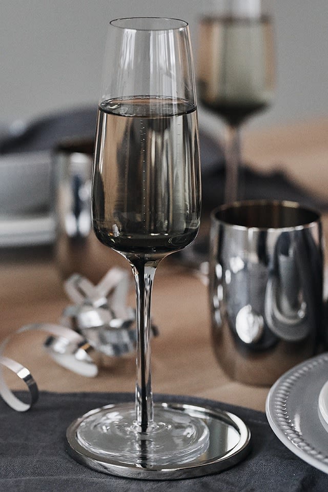 Rökfärgat champagneglas från Broste Copenhagen står på denna stilrena nyårsdukning i silver och grått. 