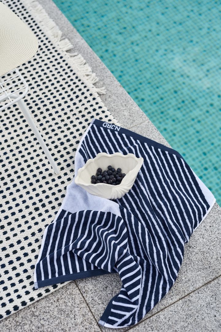 Blå handduk från NJRD och snäckskål från By On bredvid en pool. 