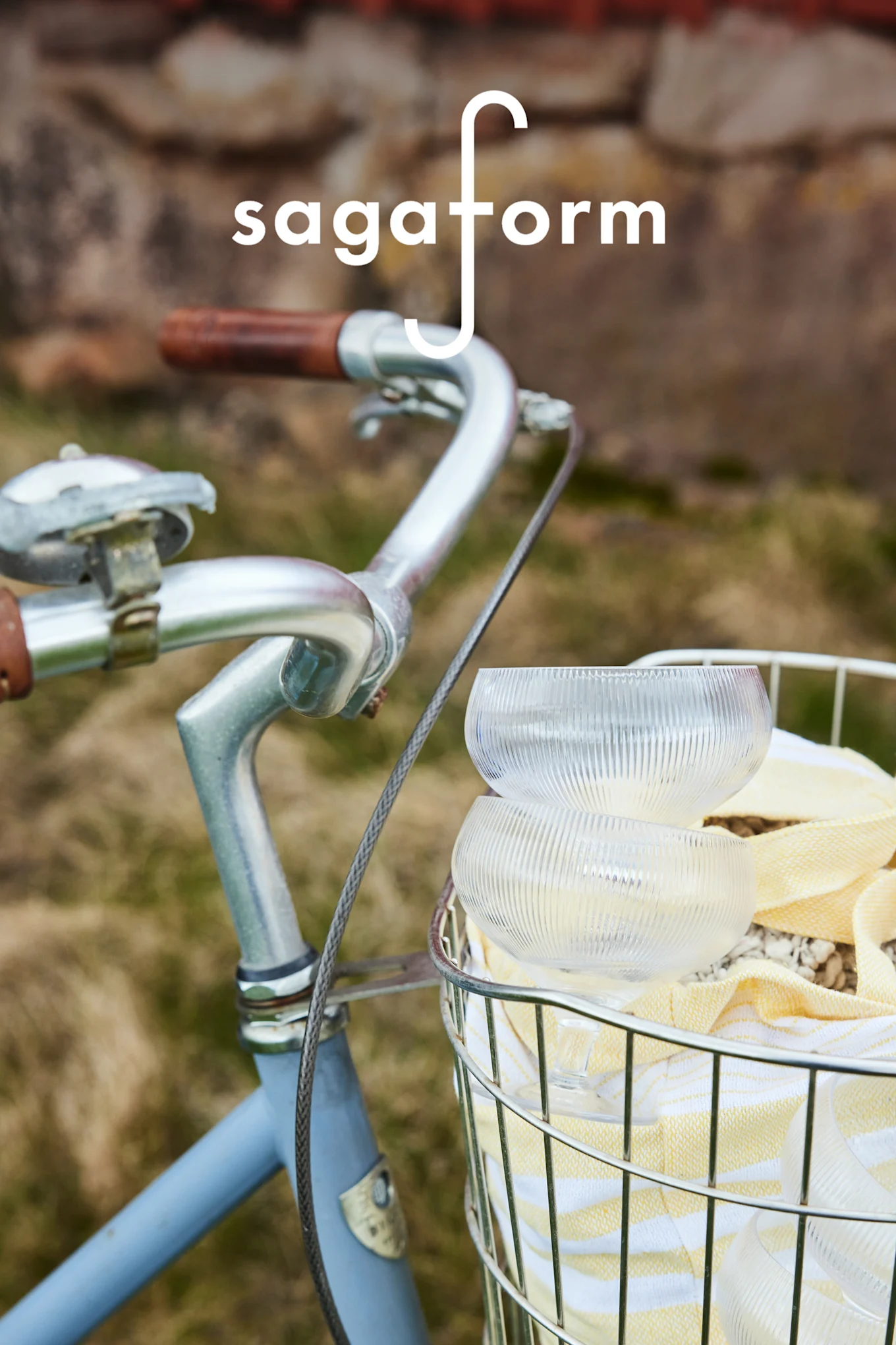 Två klara, räfflade glasskålar och en gulrandig handduk i en cykelkorg. 'sagaform'-logotyp.