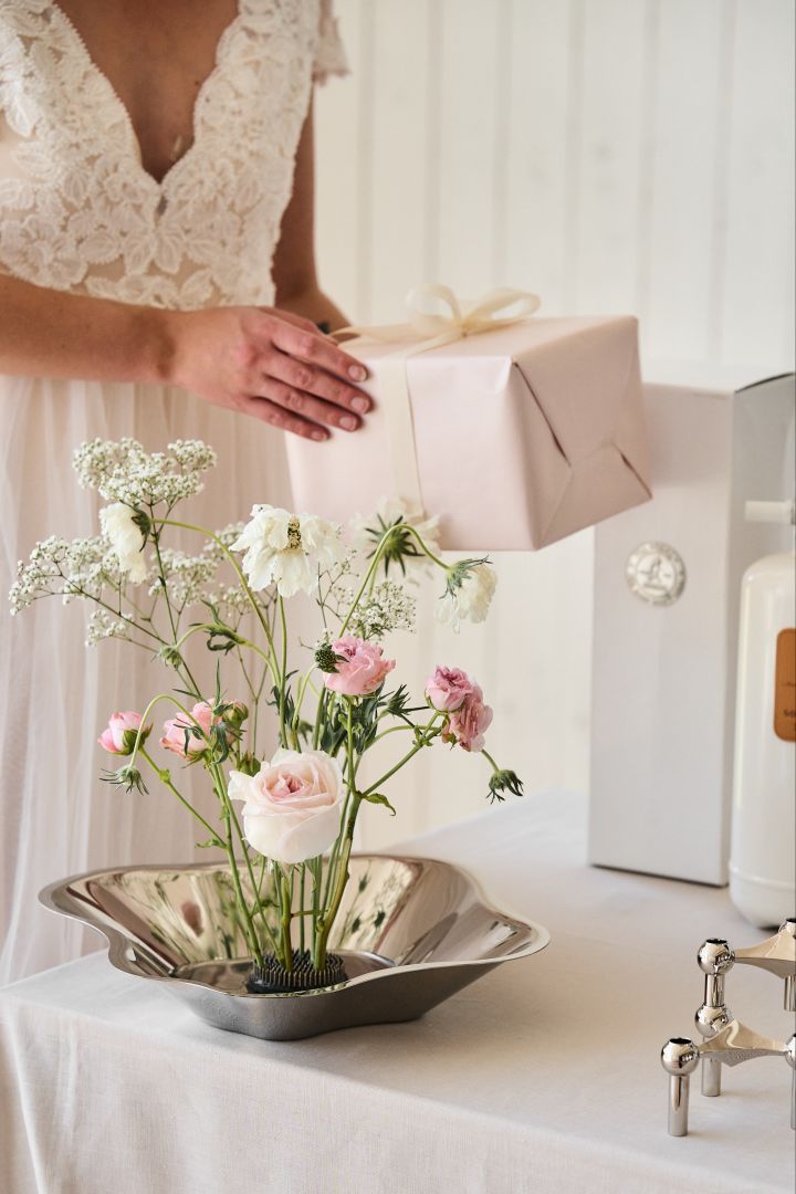 Alvar Aalto skål i rostfritt stål med blommor stående i en blomsterfakir på ett romantiskt dukat presentbord på bröllop. 