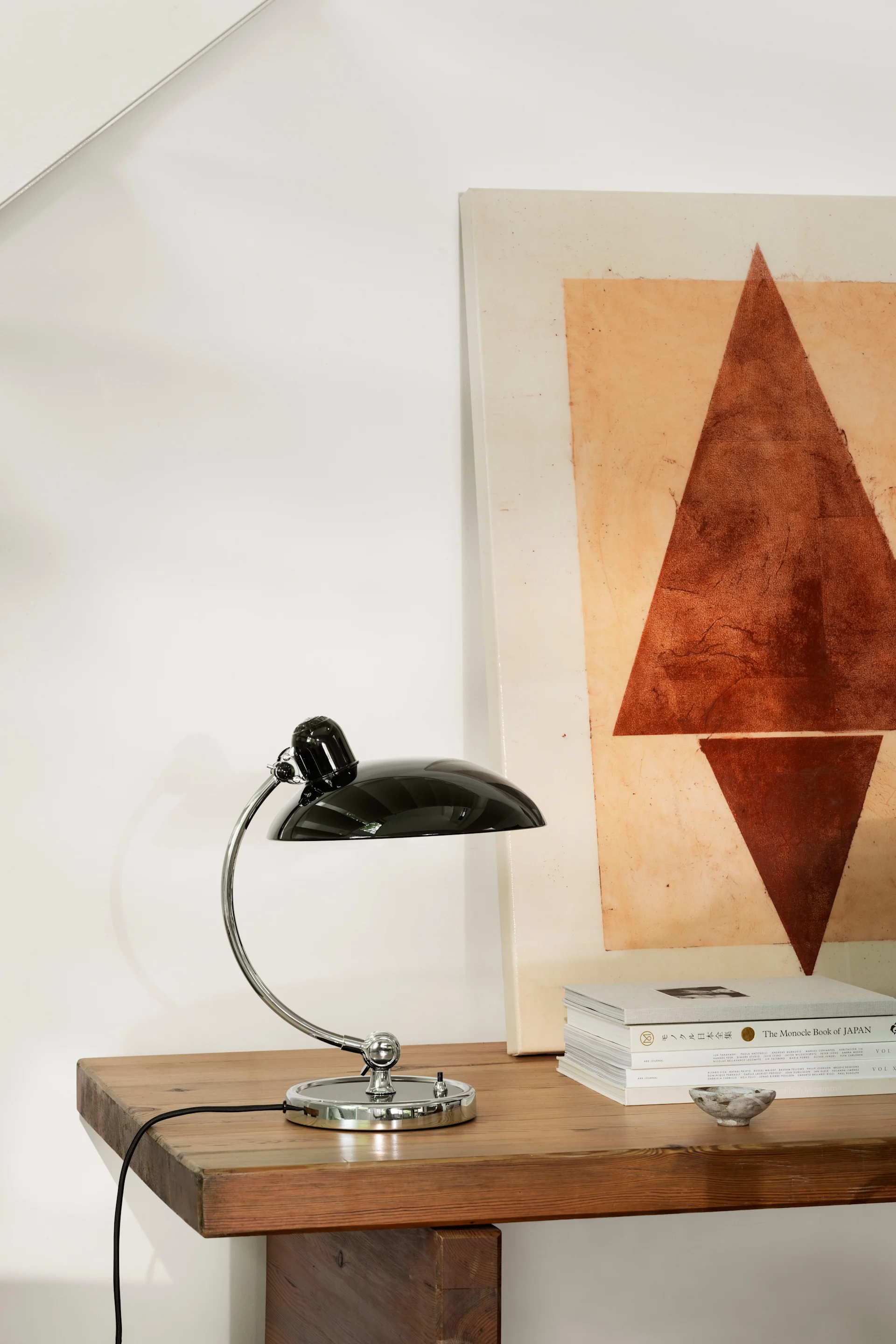 En svart Kaiser Idell bordslampa som står på ett sidobord. Lampan är en klassisk designlampa.