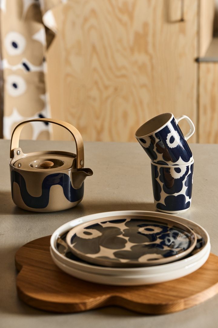 På ett bord ligger tre olika tallrikar i Mariemekkos Unikko-mönster, två muggar i samma mönster och en Seireeni tekanna i färgen terra-mörkblå. 