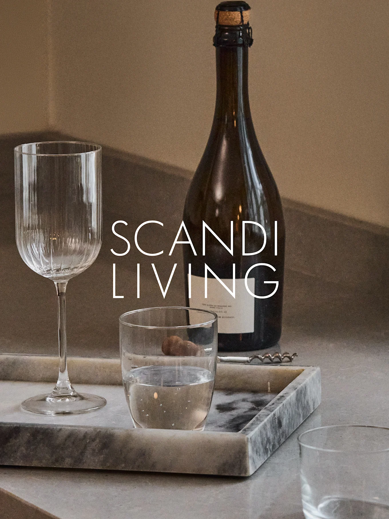 En mörk flaska, ett räfflat vinglas, ett vattenglas och en korkskruv på en marmorbricka med texten 'SCANDI LIVING'.