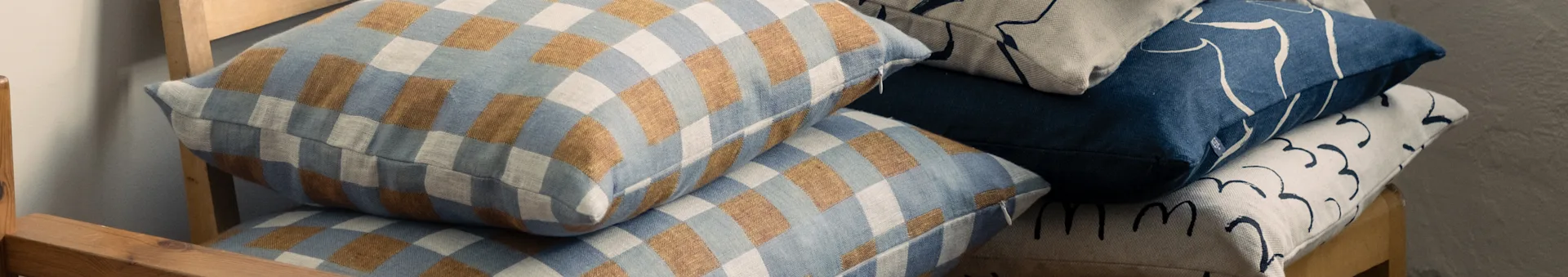 Staplade kuddar på en trästol, med rutiga blå och bruna, samt abstrakt mönstrade blå och beiga designer.