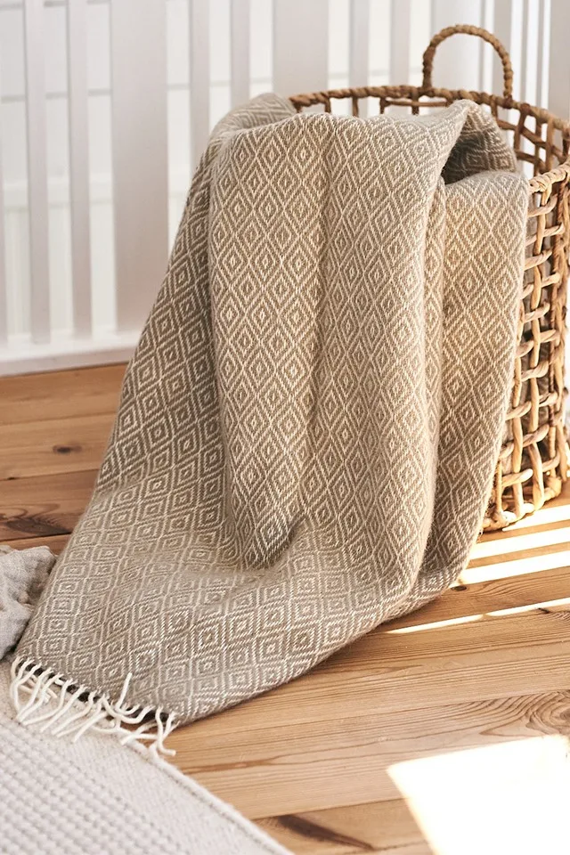 Stella beige ullpläd från Klippan Yllefabrik vilar i flätad korg från ERNST – redo för härligt hygge-mys.