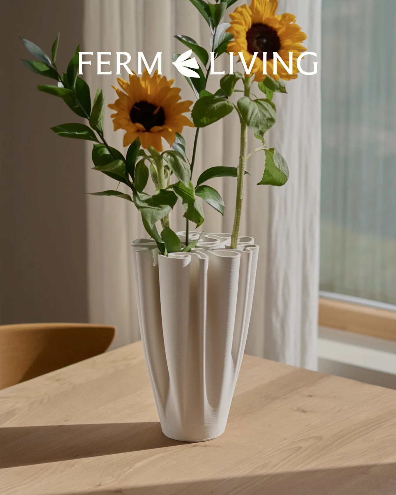 Solrosor i en vit, räfflad vågig vas på ett träbord. Ferm Living logotyp.