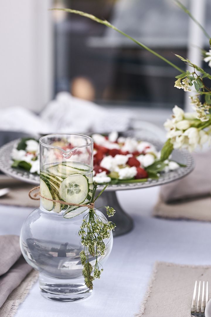 Snygg vattenkaraff från Ro Collection piffad med ängsblommor och fylld med vatten och gurka står på bordet. 