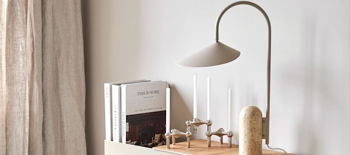 Förnya ditt hem med trendiga lampor - här ser du Arum bordslampa från Ferm Living i toner av beige och marmor bredvid Stoff Nagel ljusstake i silver på Plant Box i beige från Ferm Living.