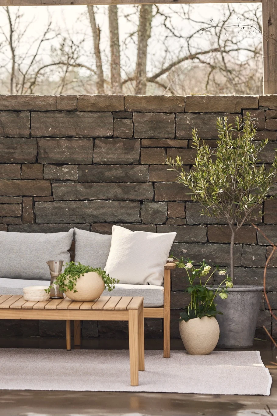 En mysig terrass med en matta, en soffa och ett sidobord, bredvid många växter.