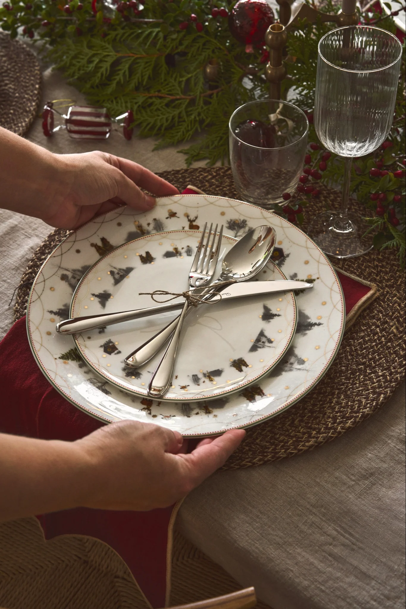 Händer som dukar ett julbord med tallrikar prydda av julmotiv, inspirerade av julens trender 2025.