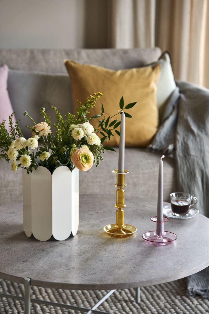 En blomsterbukett i vita Arcs vas bredvid Pirouette kopp med fat och Flare ljusstakar i gult och rosa från HAY.