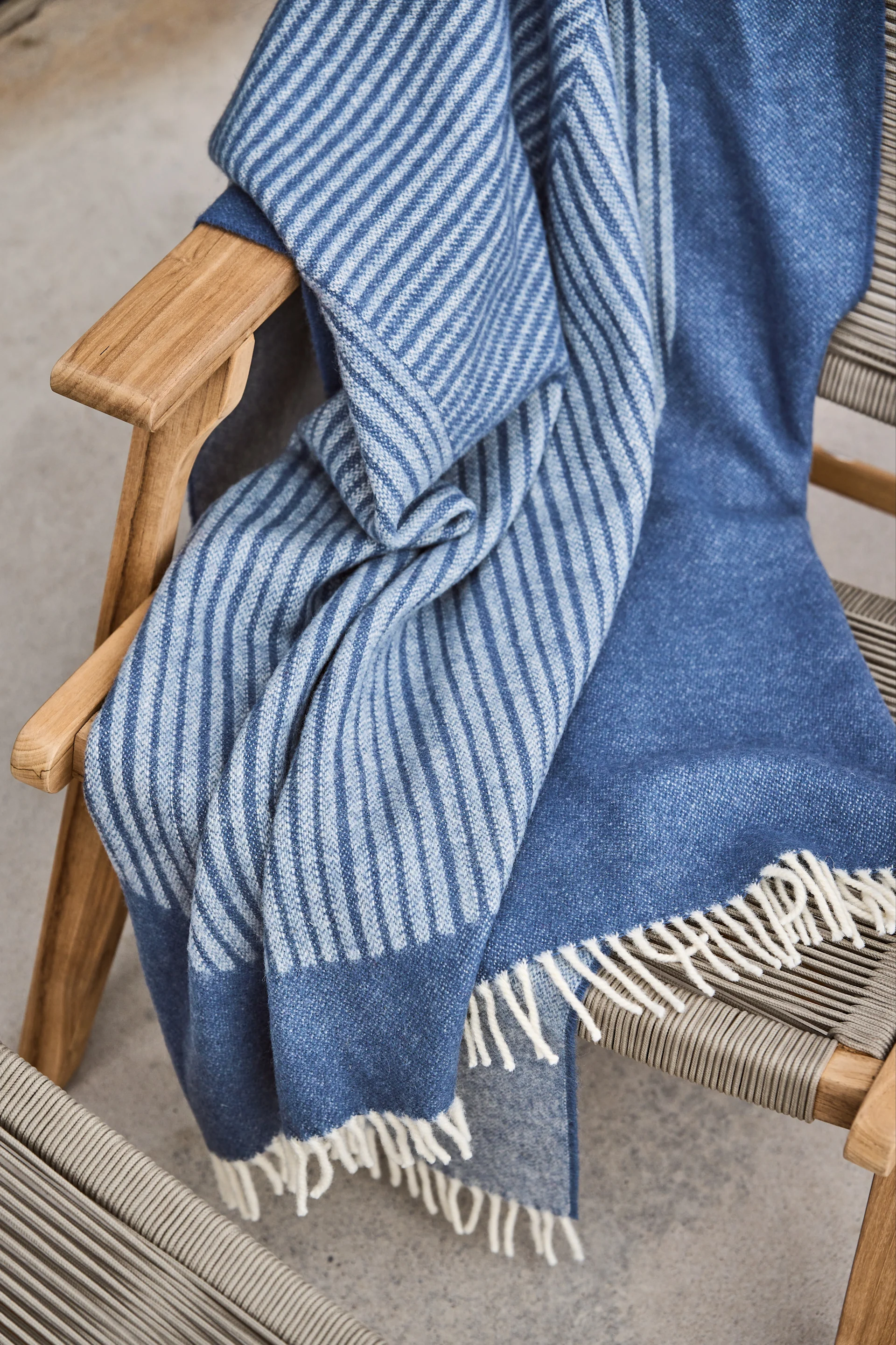 Stripes ullpläd från NJRD i en blå färg med randigt mönster ligger över en stol i trä.