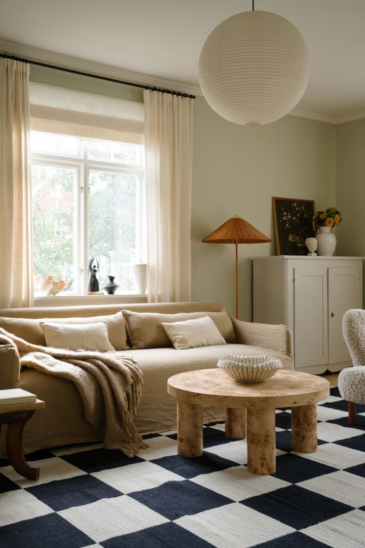 Bild som visar Rice paper lampskärm från HAY, här hängandes i vardagsrum med beige soffa, svart-vit-rutig matta och rustikt soffbord i trä.