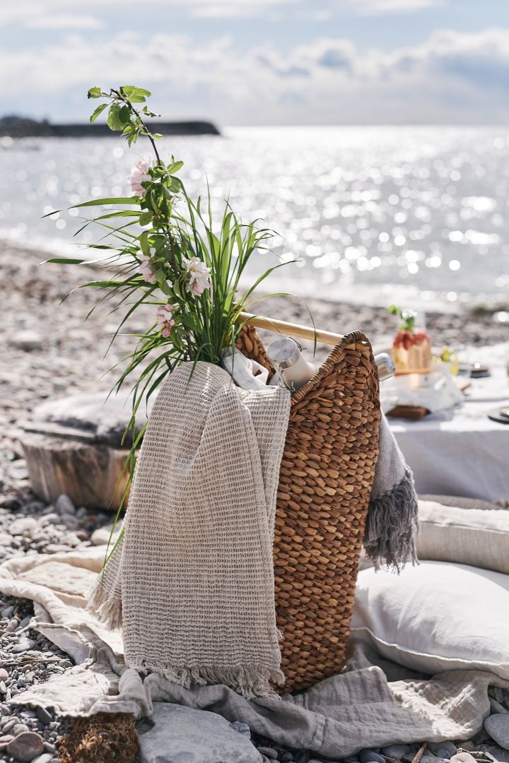 Picknickkorg packad med plädar och termos för en picknick på stranden. 