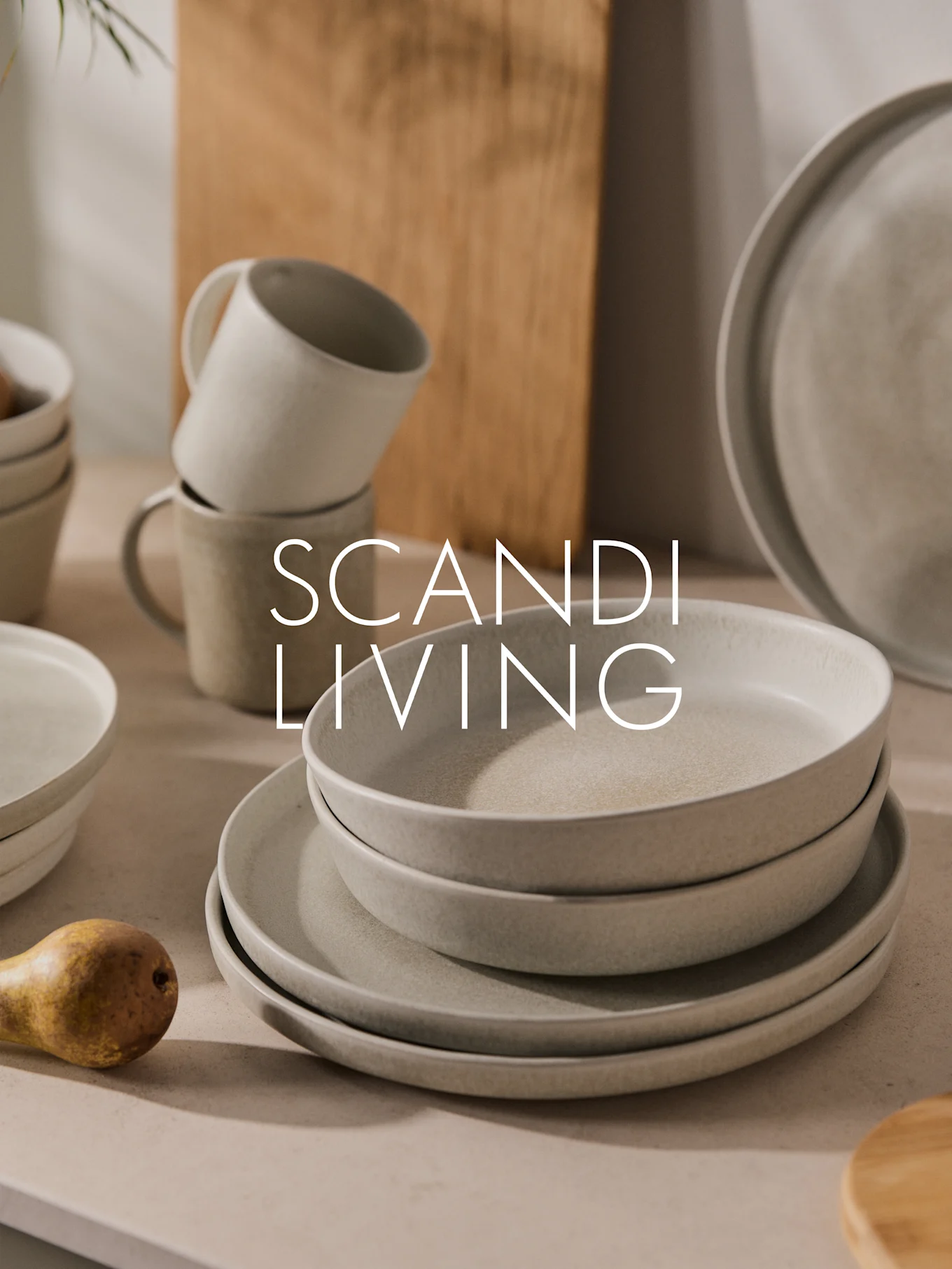 Stapel med ljusa, spräckliga keramiktallrikar, skålar och muggar med ett päron. Text: SCANDI LIVING.