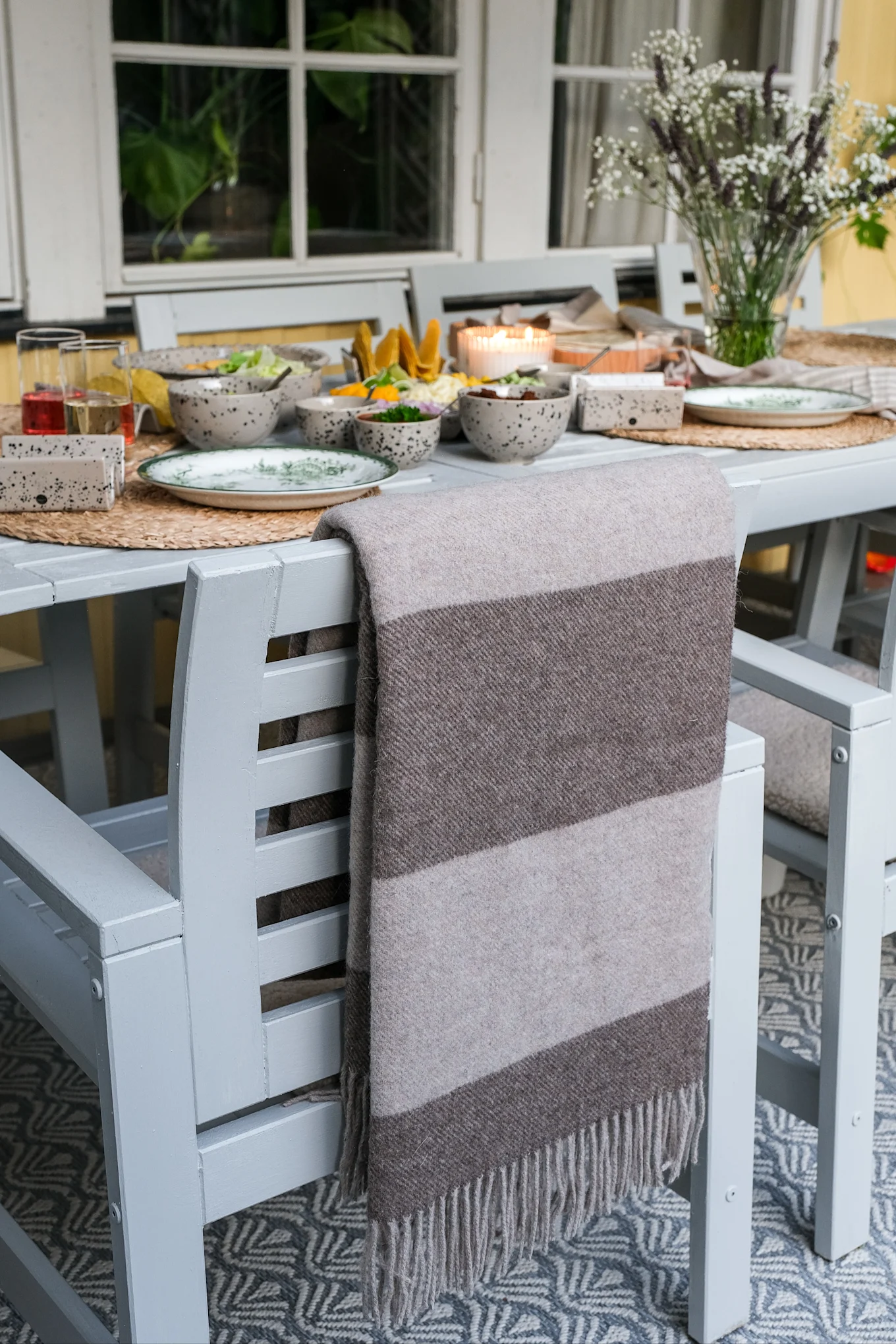 För en mysig vardagsmiddag utomhus, häng en värmande pläd över stolen. Här Ulle ullpläd i beige och brunt med breda ränder och fransar.