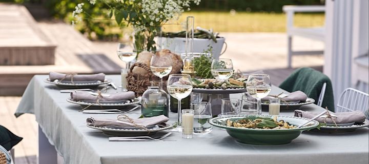 En sommardukning med tema grönt står uppdukat på verandan för härlig trädgårdsfest.