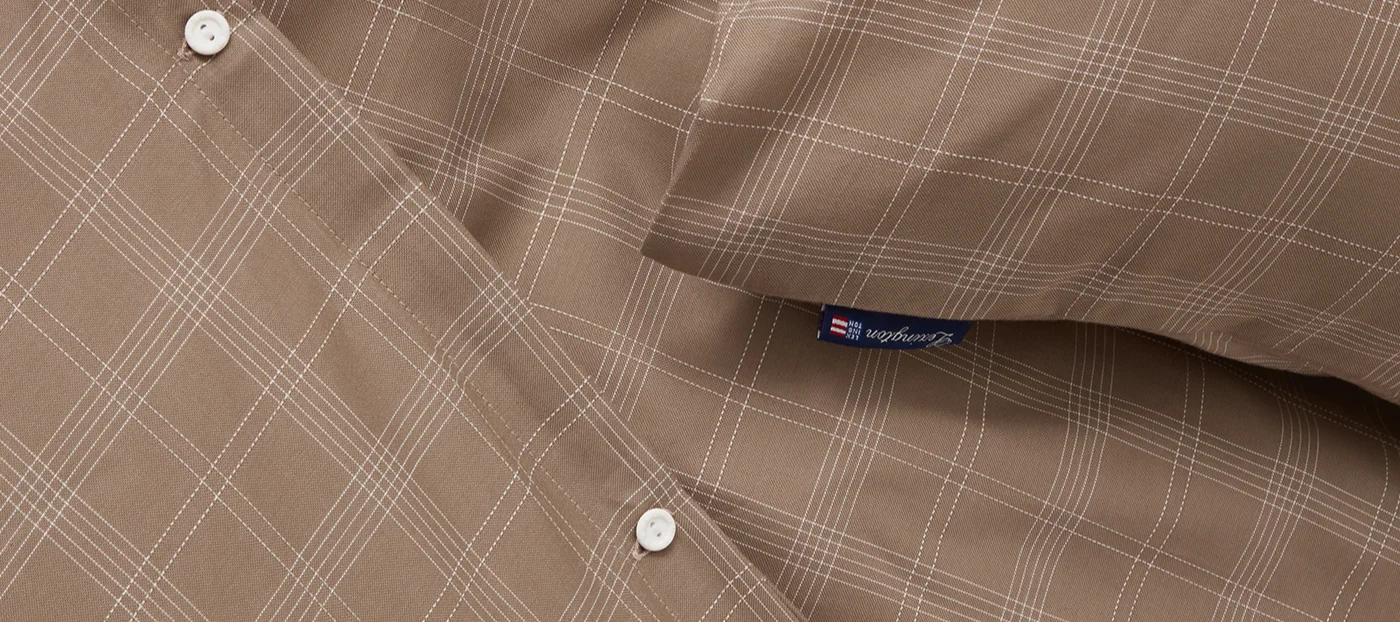 Närbild av brunt tyg med vitt rutmönster, med två vita knappar och en blå Lexington-etikett.