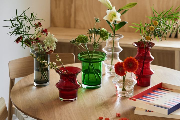 Kollektion av Pagod och Limelight vaser från Kosta Boda i olika storlekar och färger som rött, grönt, grått och klarglas på ett ekbord. 