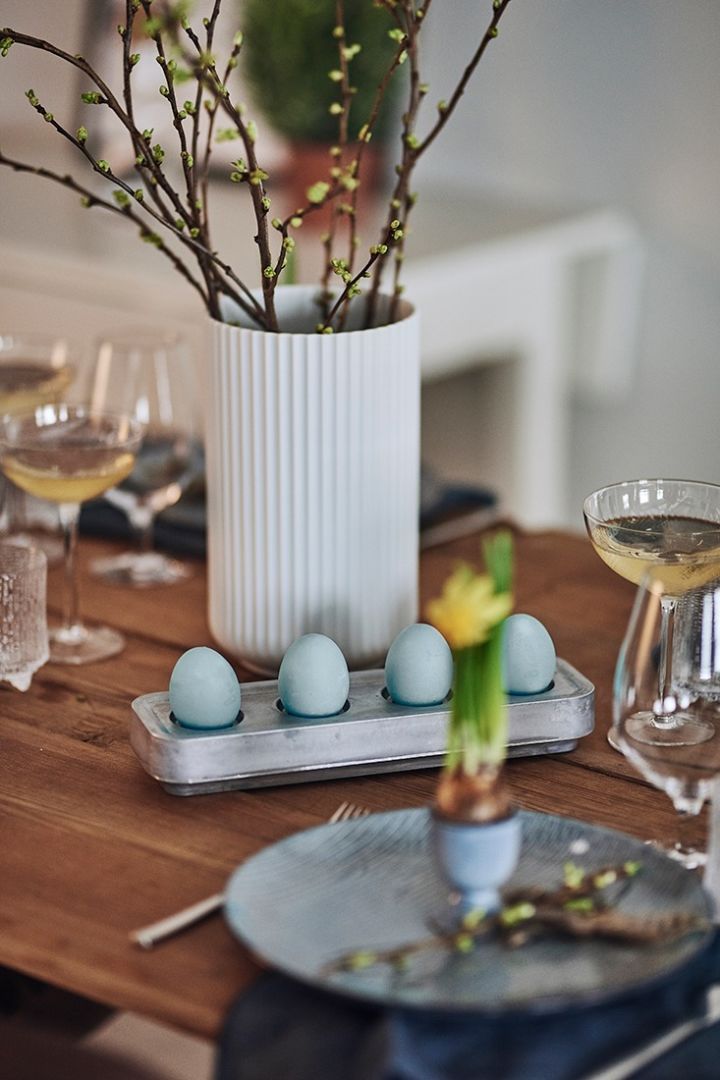 Duka till påsk med färgade, blå ägg på bordet som här där de får sitta i en ljusstake.