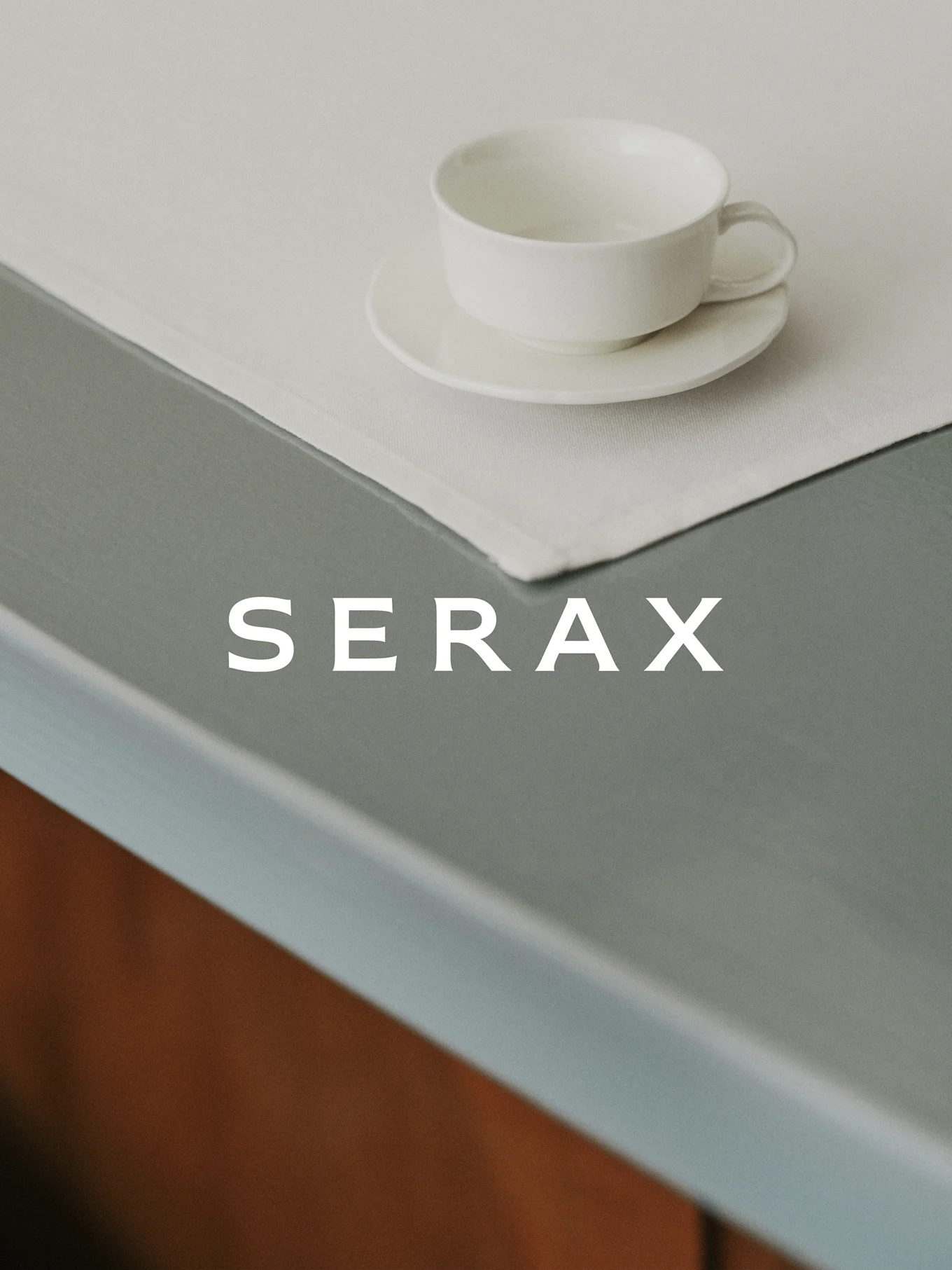 En vit tekopp och fat på en ljus linneservett på ett grått bord med ordet SERAX.