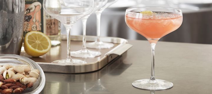 En mocktail med grapefruktjuice i ett Cabernet-cocktailglas från Holmegaard står på en köksbänk med cocktailredskap i bakgrunden.