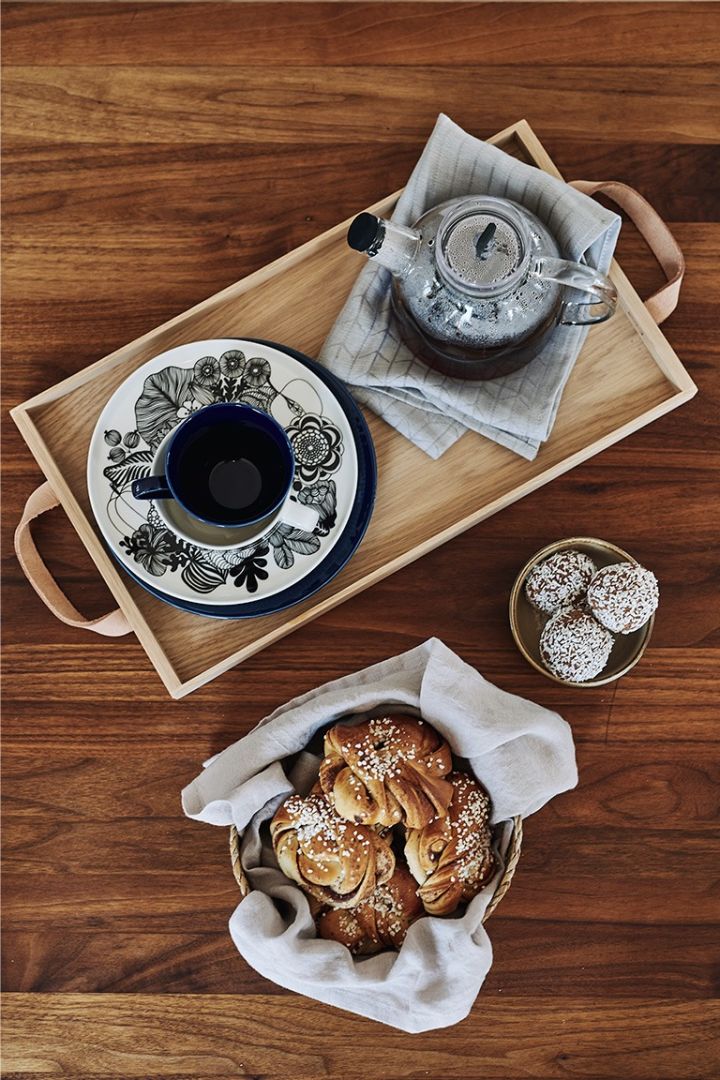 En klassisk svensk fika står uppdukad på träbricka i köket med kaffe, kanelbullar och chokladbollar. 