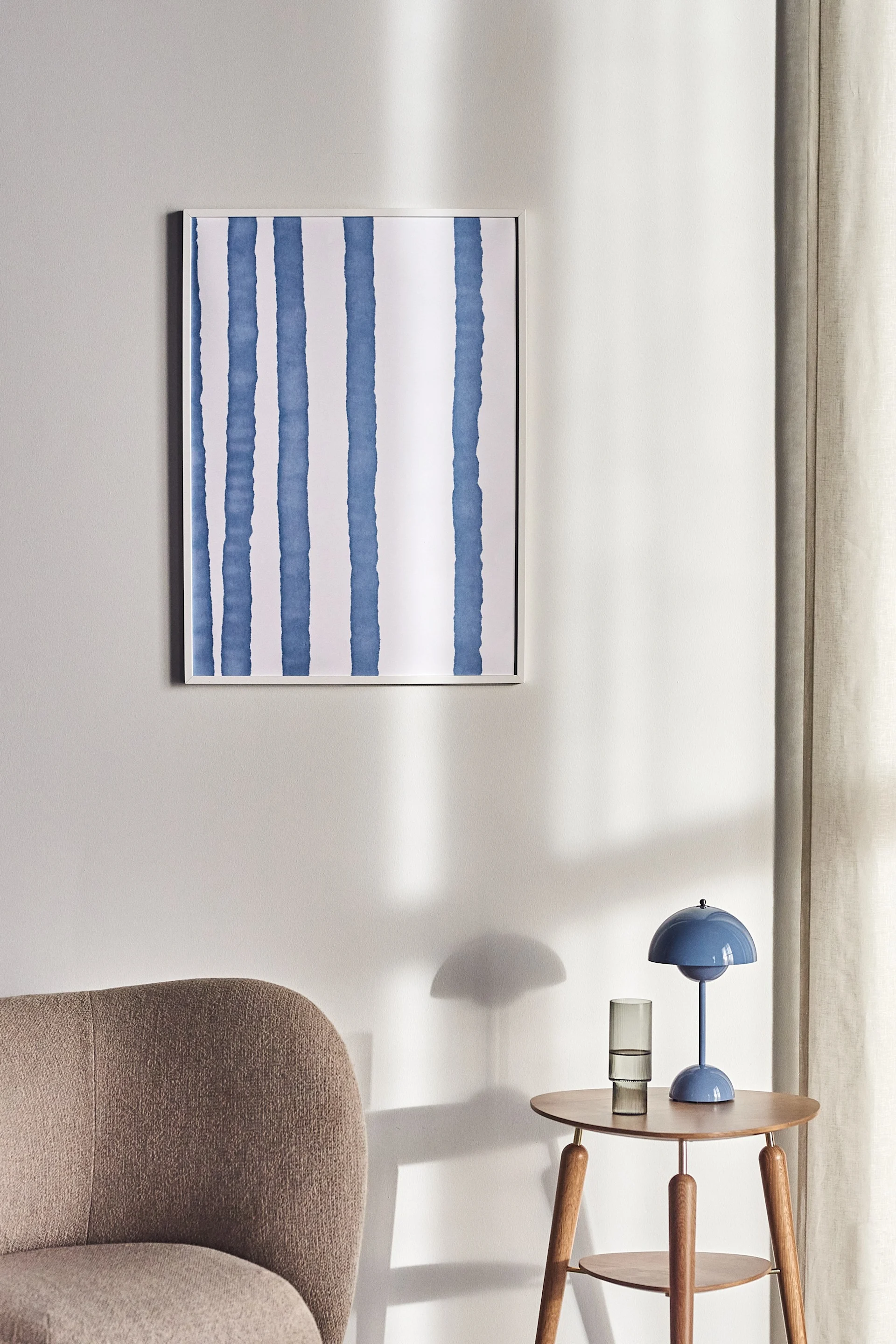 Lineage poster från  Scandi Living sitter upphängd mot en naturvit vägg. Postern är vit med blåa organiska ränder. 