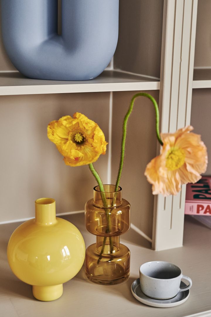 Färgtrender 2023 - inredning som går i varma gula toner av bärnsten och pastellgult. Här i små vaser på bokhyllan. 