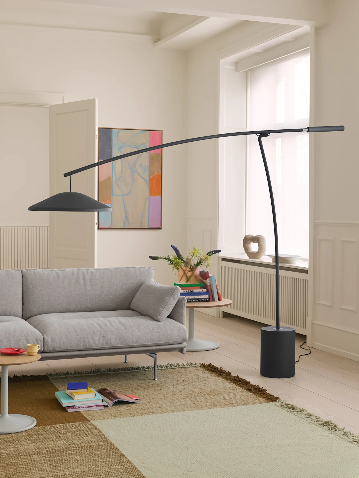 Modernt vardagsrum med ljusgrå soffa, mörkgrå böjd golvlampa och en mönstrad matta på ljust trägolv.