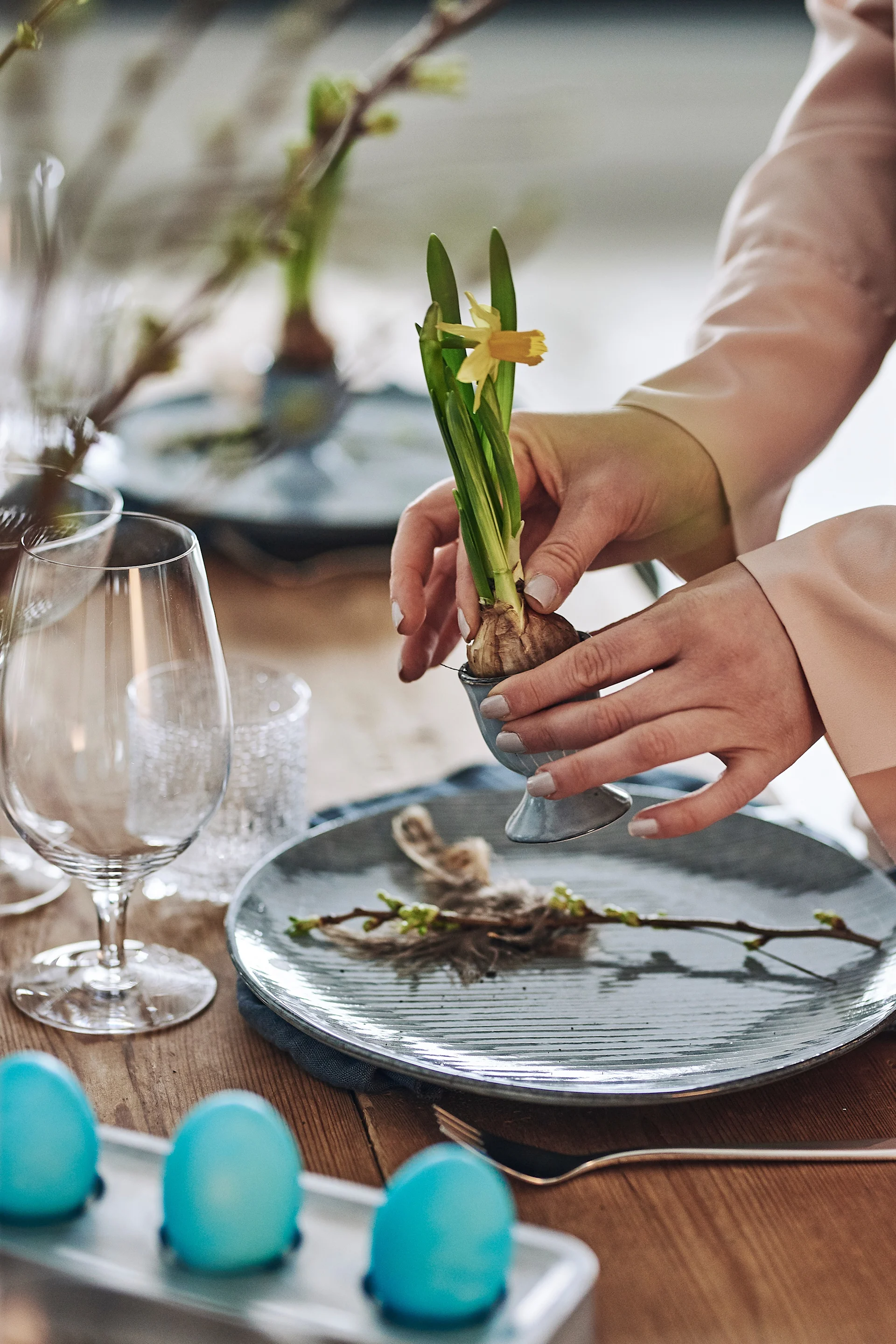 Små påskliljor sätts i äggkoppar från Broste Copenhagen och placeras på påskdukningens tallrikskuvert som en söt välkomsthälsning till bords.