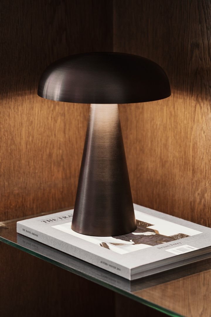&Tradition Como portabel bordslampa i mörkbrun färg i bokhylla i mörka träslag - komponenter som speglar höstens inredningstrender 2021.