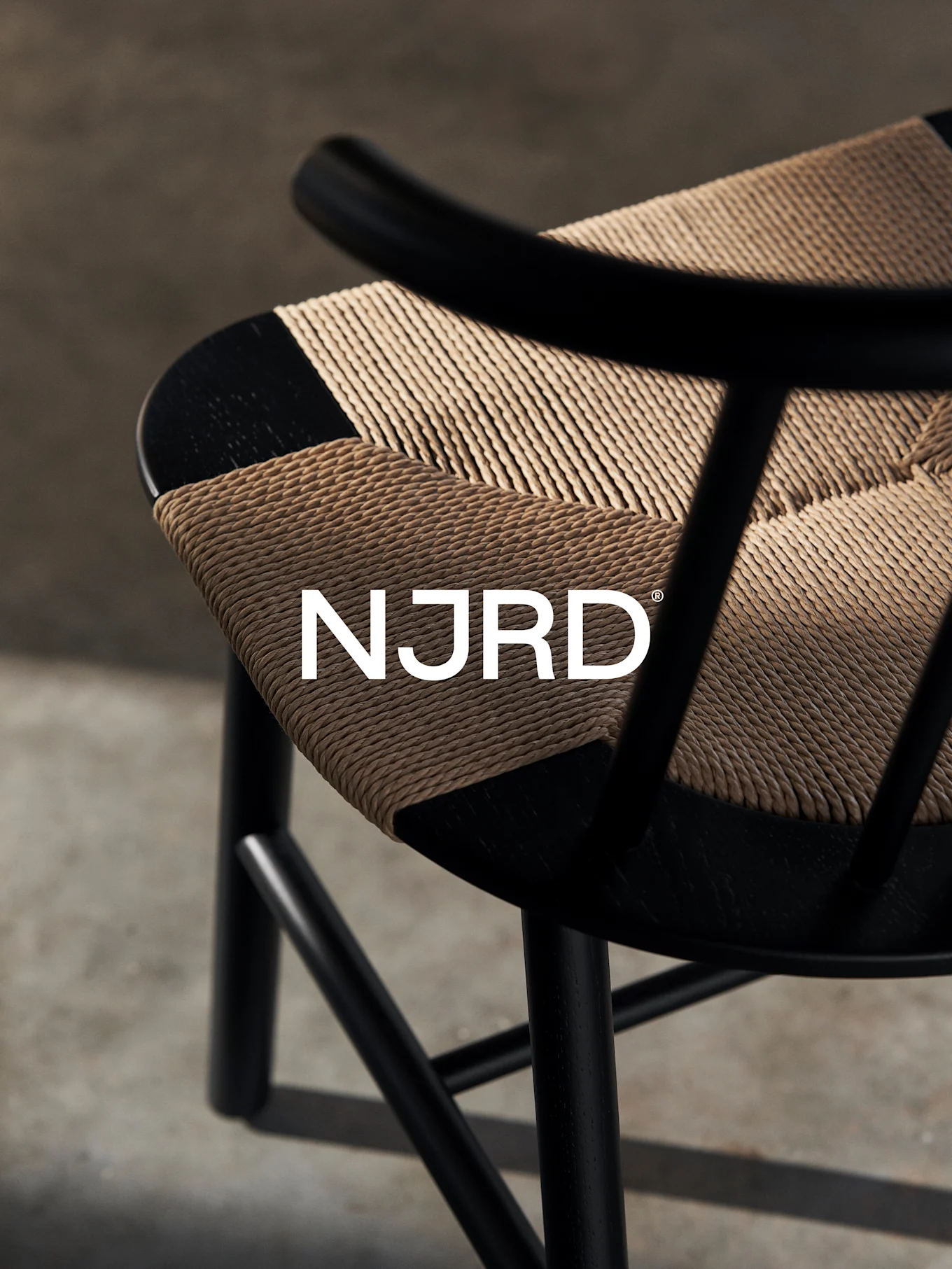 Närbild av en svart stol med en vävd ljusbrun sits, med den vita 'NJRD'-logotypen.