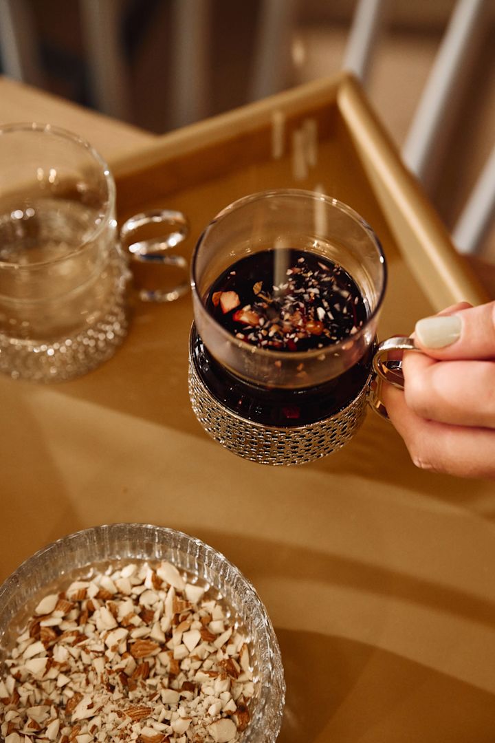 Någon strösslar mandel i ett glas fyllt med glögg. 
