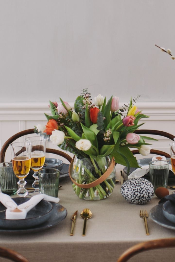 En färgsprakande tulpanbukett står på bordet som vacker och naturlig dekoration på en fin påskdukning. 