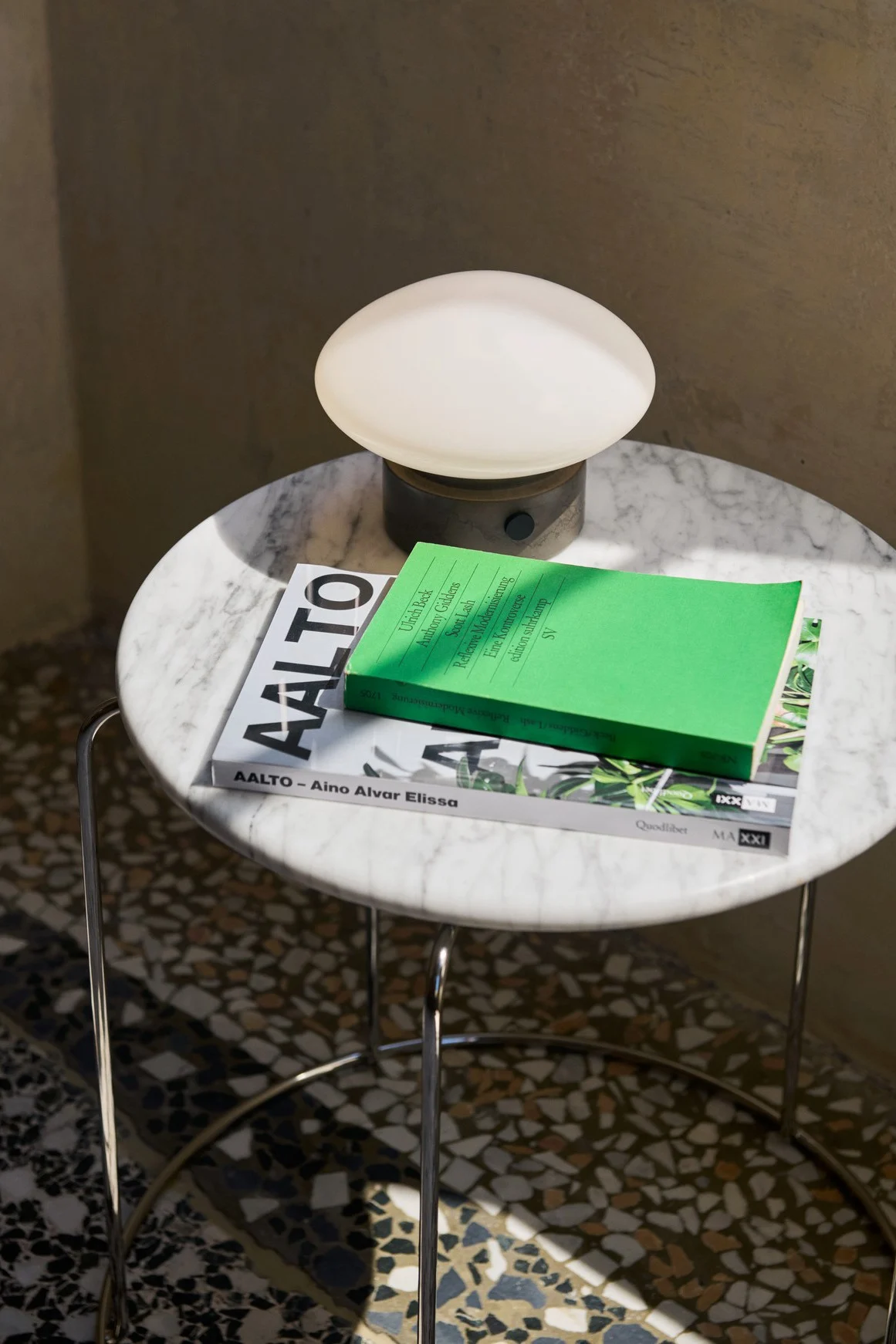 Mist AP12 portabel lampa från &tradition står på ett litet runt marmorbord tillsammans med böcker. 
