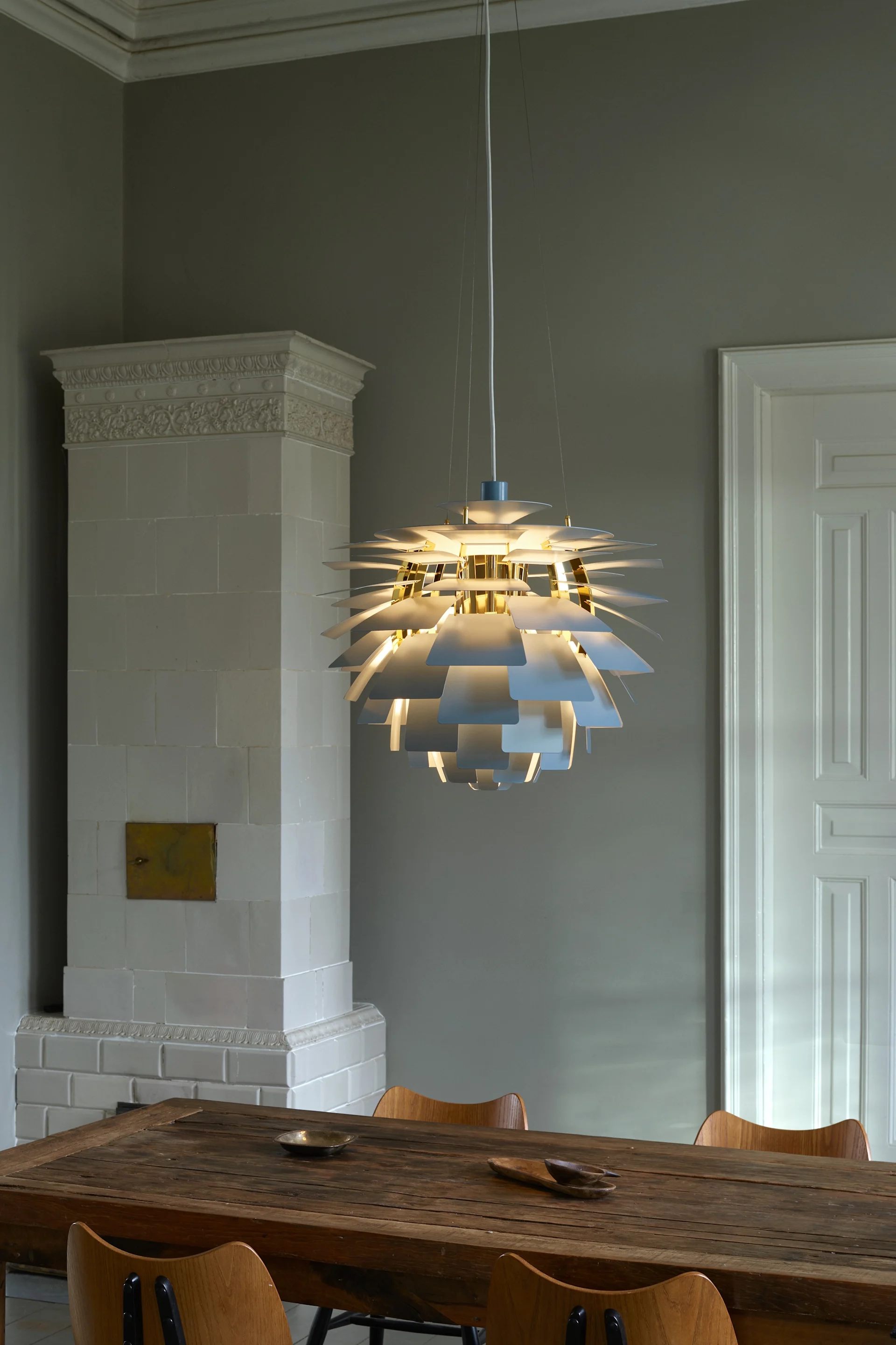 En strålande flerskiktad taklampa med vita och gulddetaljer som lyser upp ett rustikt trämatbord.