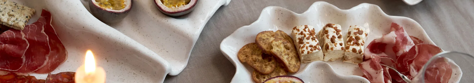 En förrättsanrättning på två snäckformade fat med charkuterier, kex, ost och passionsfrukt, med ett tänt ljus.