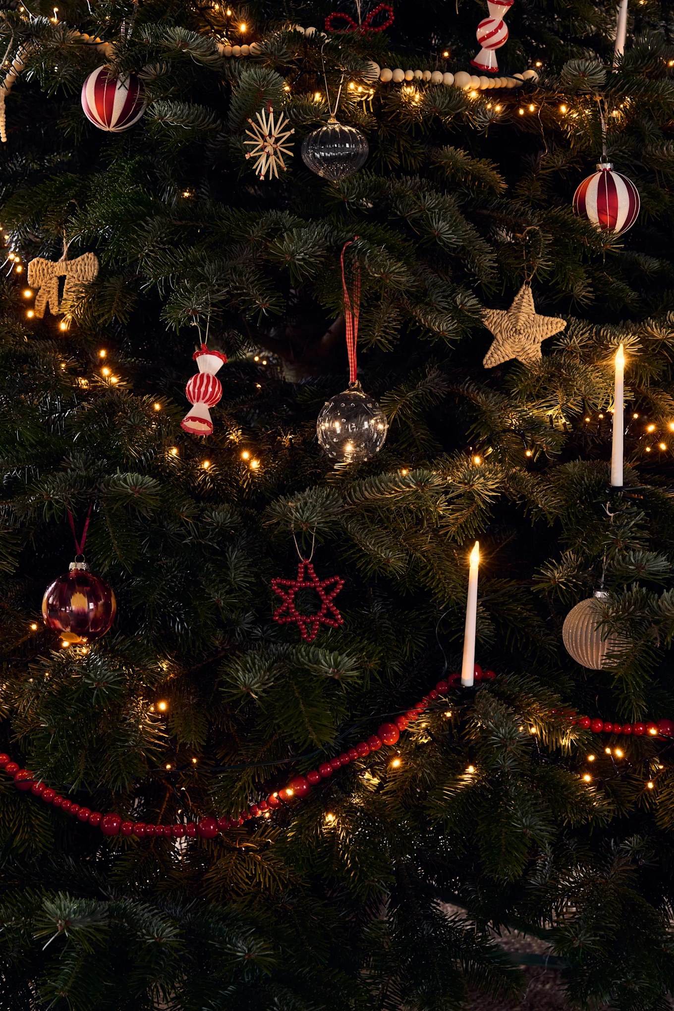 En rikt dekorerad julgran med olika ornament, varma ljusslingor och glödande ljus.