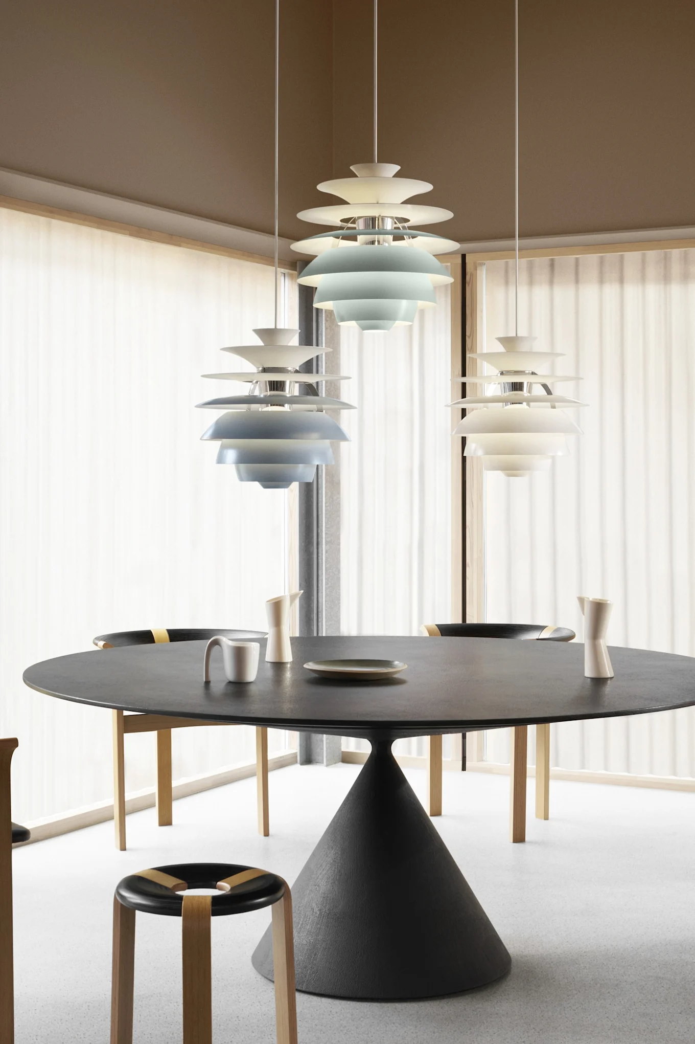 Modernt matrum med runt svart bord, stolar och tre skiktade pendellampor, två blå och en vit.