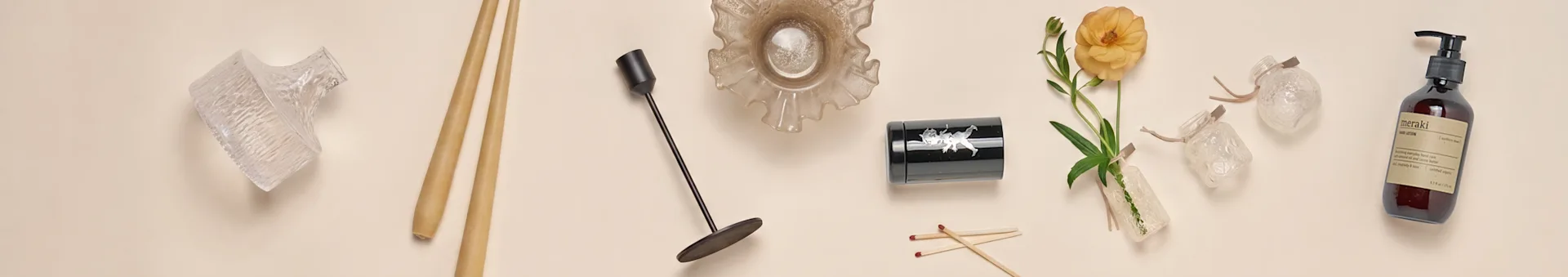 En samling heminredningsartiklar, inklusive glasvaser, ätpinnar, en svart ljusstake, en ruffsig glasskål, en svart behållare, en orange blomma och en handlotionflaska.
