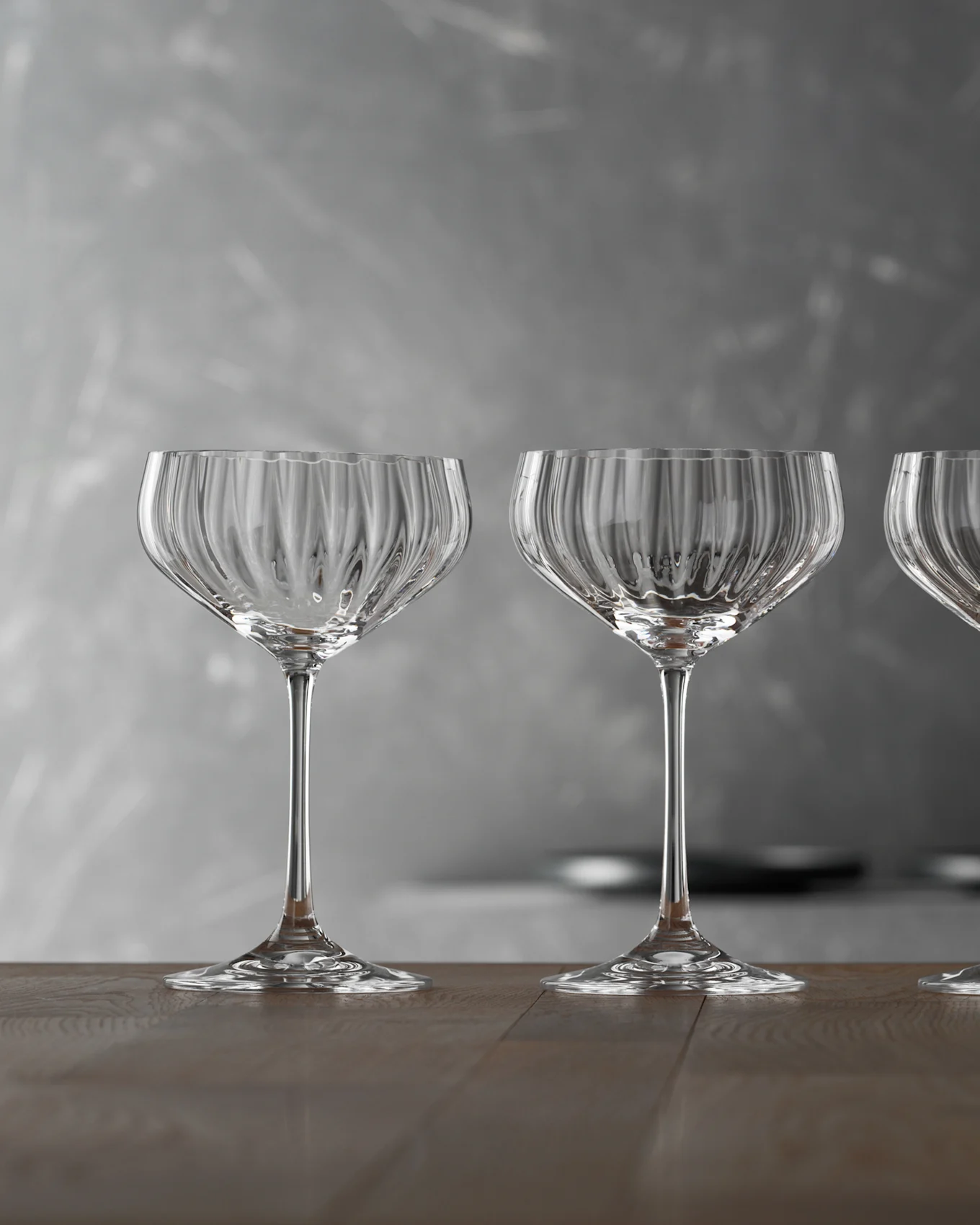 Tre tomma, klara räfflade champagneglas på ett träbord mot en grå bakgrund.