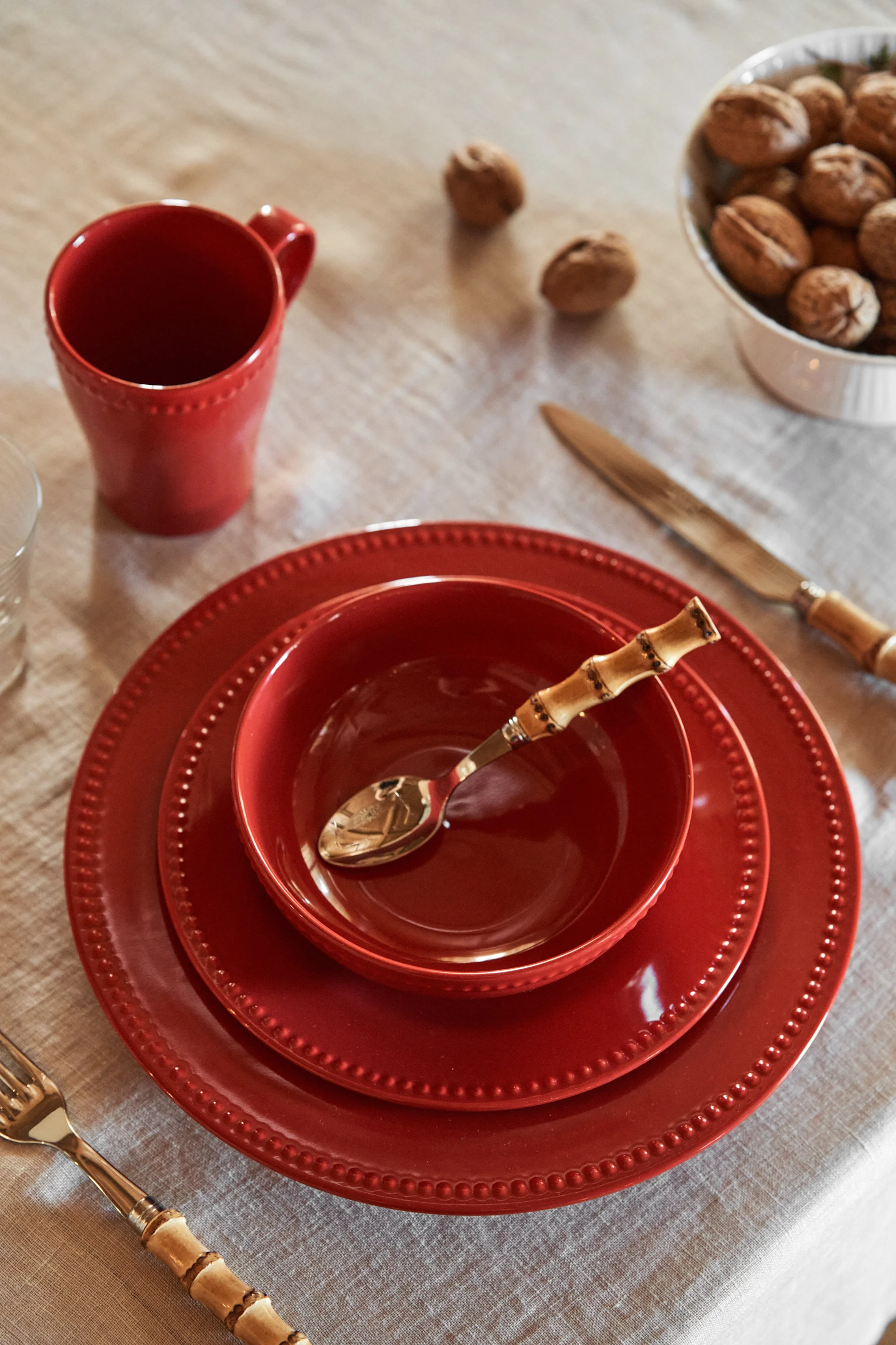 Ett avskalat rött porslin med tallrikar i olika storlekar, kombinerat med en skål fylld med valnötter – en stilren tolkning av juldukningen 2025