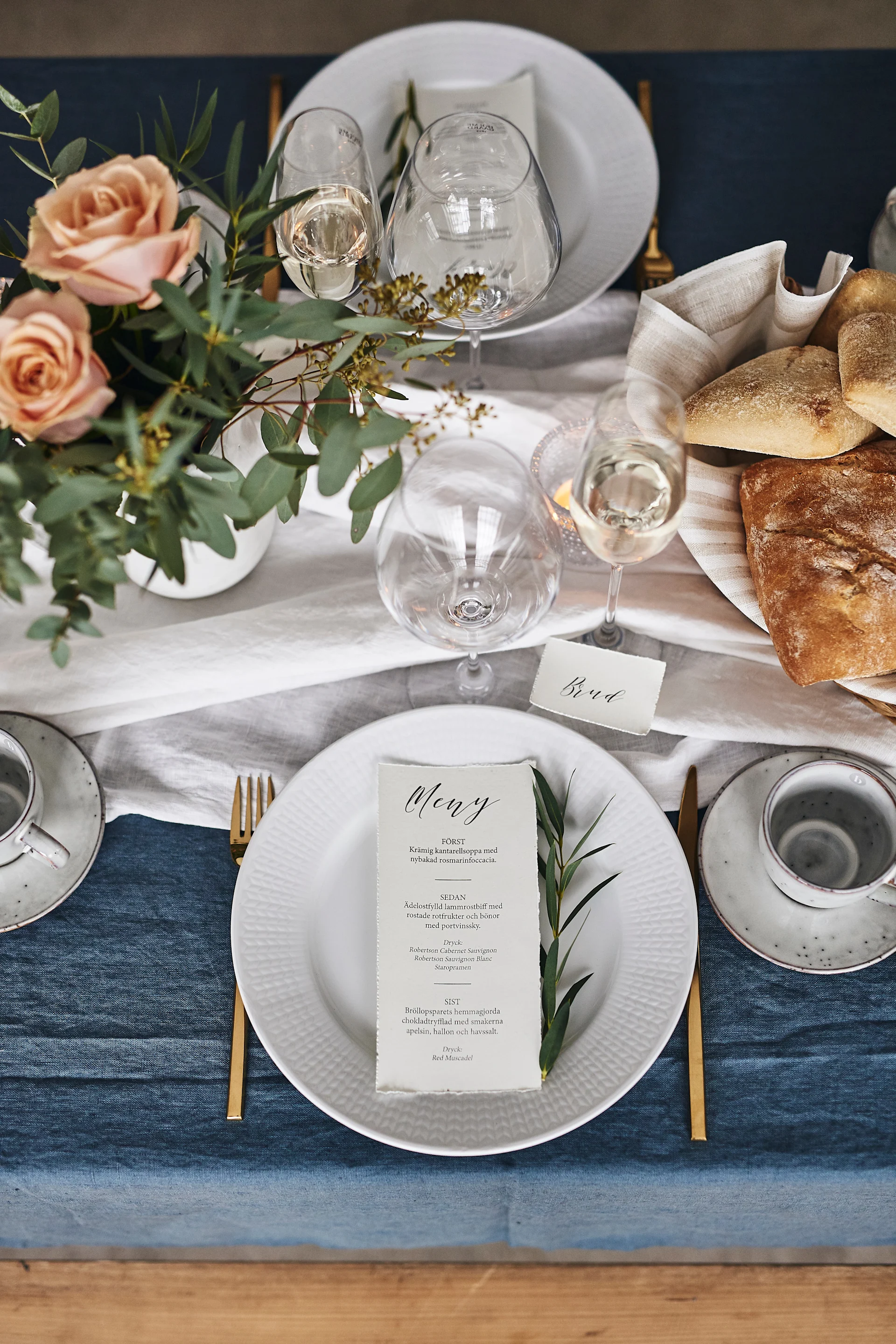 Bröllopsdukningens kuvert med vita Swedish Grace tallrik med mässingbestick och eleganta glas från Holmegaard.