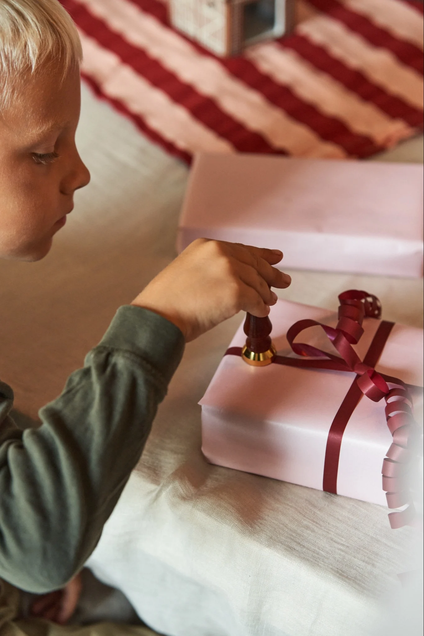 Det är första advent och en pojke sätter en stämpel på en julklapp inslagen i rosa papper och rött presentsnöre.