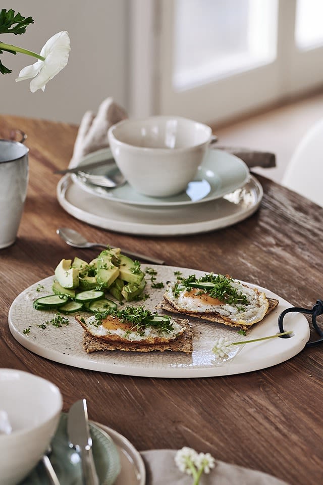 Äggmacka och avokado står serverat på bordet på en vit skärbräda från Lene Bjerre. 