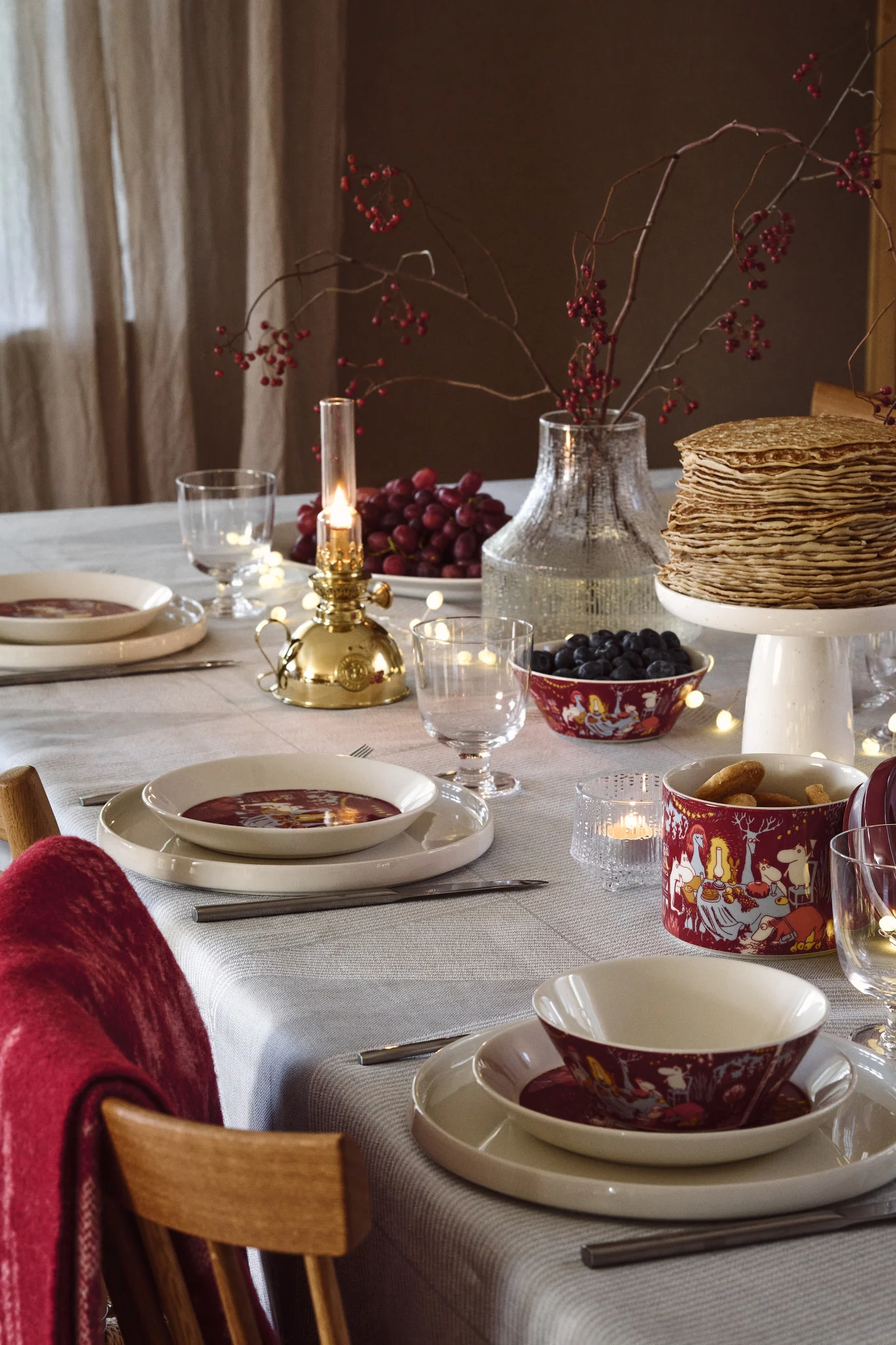 En lekfull juldukning 2025 skapas med rött porslin prytt med Muminmotiv, kombinerat med färgglada bär som sätter en varm och inbjudande ton på bordet.