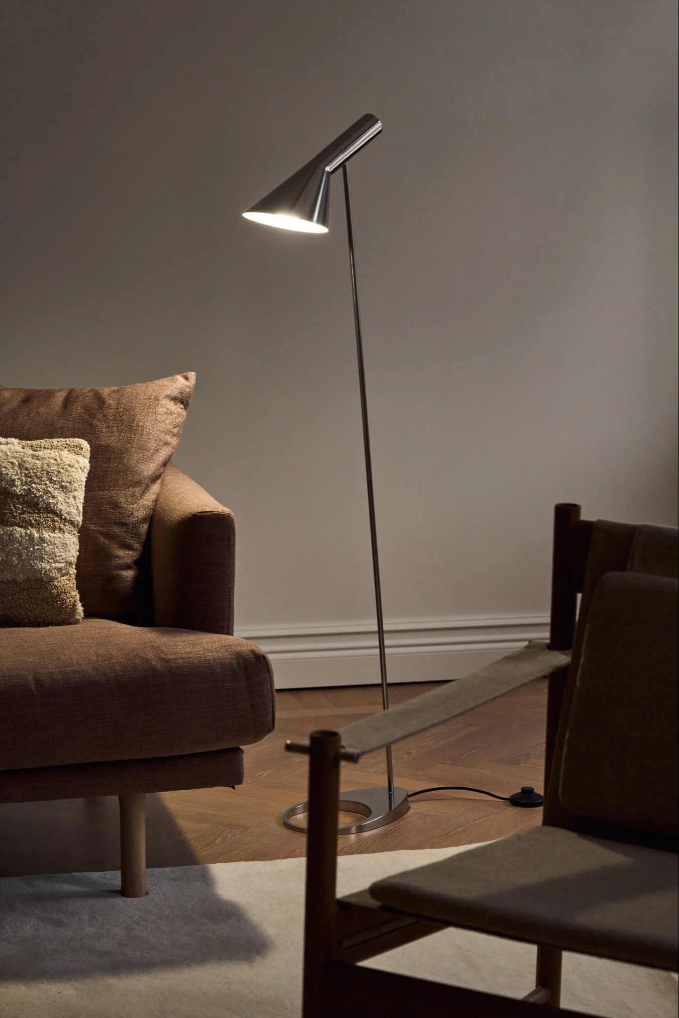 En AJ golvlampa i rostfritt stål finns i ett vardagsrum och visar på en klassisk designlampa. 