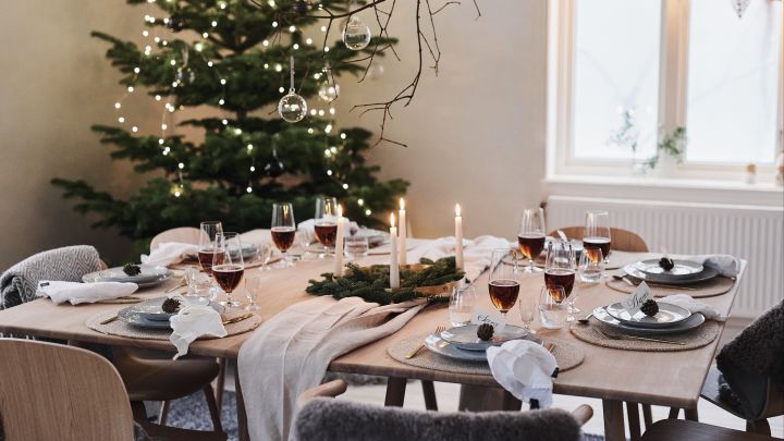 En vit och minimalistisk juldukning inväntar årets julmiddag med naturliga dekorationer som kottar och granris på bordet. 