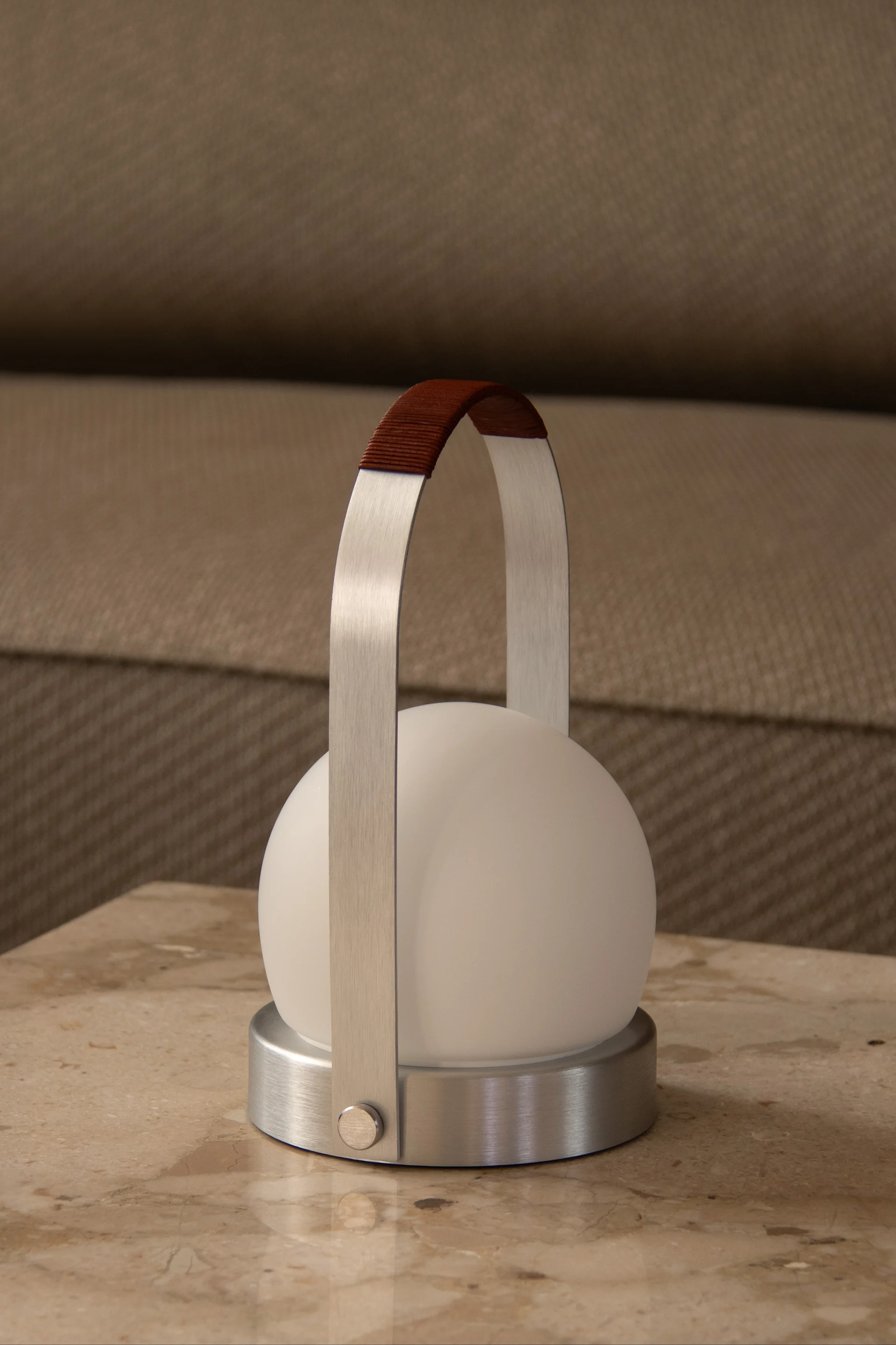 En modern bärbar lampa med vit sfärisk diffusor, borstad metallbas och ett handtag insvept i brunt material.